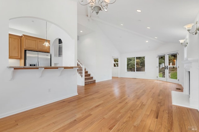 unfurnished living room with a notable chandelier, light hardwood / wood-style floors, and high vaulted ceiling