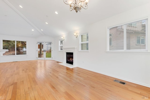 unfurnished living room featuring an inviting chandelier, vaulted ceiling, and light hardwood / wood-style floors