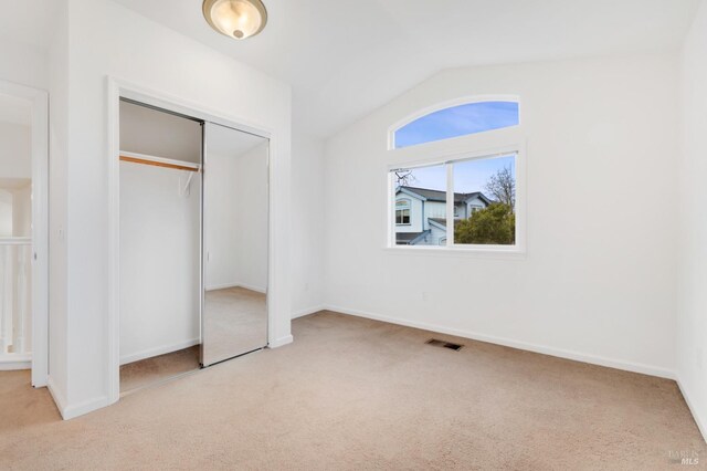 unfurnished bedroom featuring vaulted ceiling, light carpet, and a closet