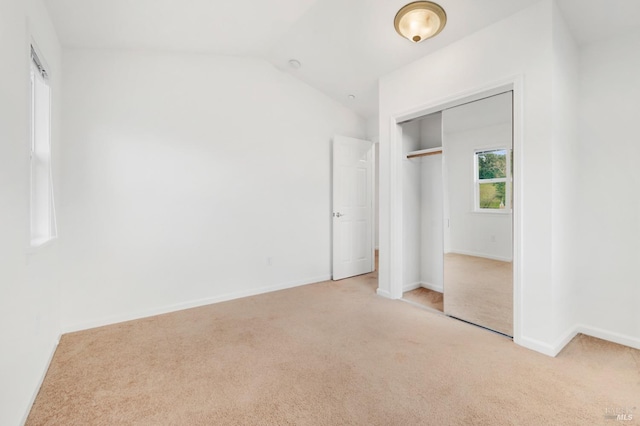 unfurnished bedroom featuring lofted ceiling, light carpet, and a closet