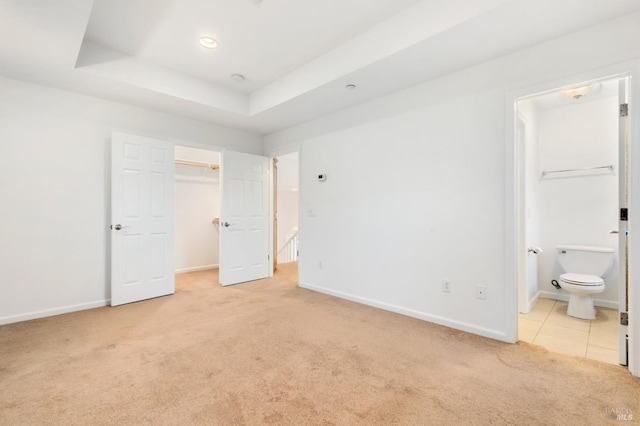 unfurnished bedroom featuring ensuite bathroom, a tray ceiling, a spacious closet, light colored carpet, and a closet