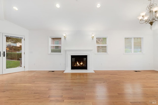 unfurnished living room featuring lofted ceiling, a wealth of natural light, a notable chandelier, and light wood-type flooring