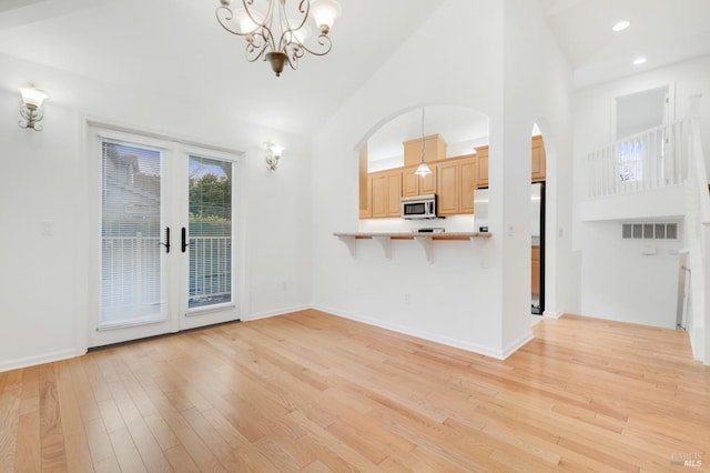 unfurnished living room featuring an inviting chandelier, high vaulted ceiling, french doors, and light wood-type flooring