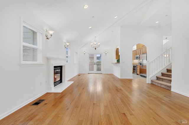 unfurnished living room with an inviting chandelier, light hardwood / wood-style flooring, and high vaulted ceiling