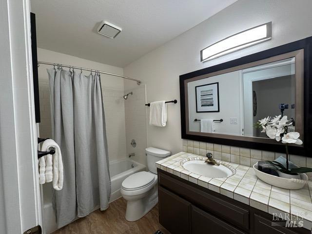 full bathroom featuring toilet, wood-type flooring, vanity, shower / bath combo with shower curtain, and backsplash