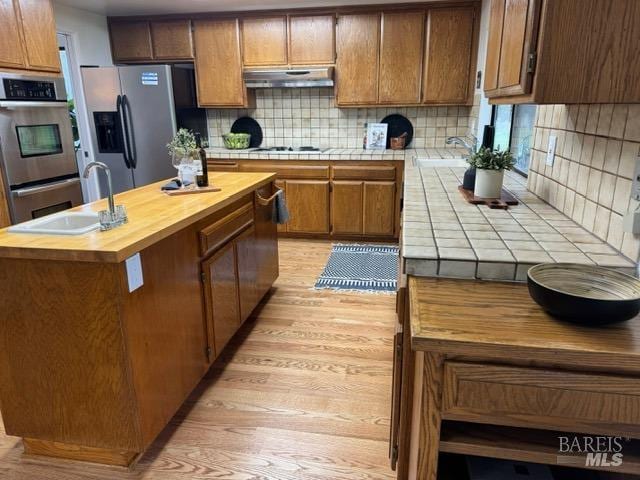 kitchen featuring a kitchen island, sink, backsplash, stainless steel appliances, and light hardwood / wood-style flooring