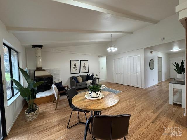 dining area with vaulted ceiling with beams, a wood stove, an inviting chandelier, and light wood-type flooring