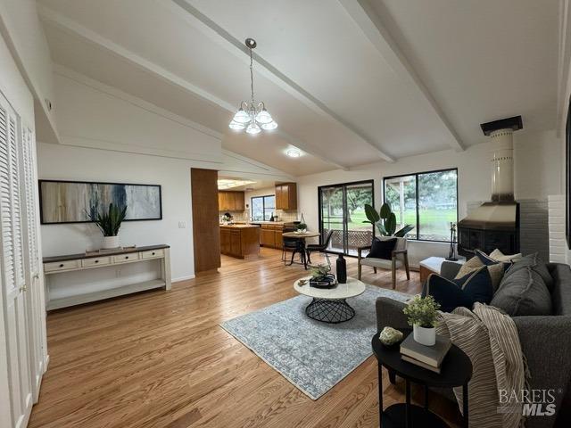 living room featuring a chandelier, lofted ceiling with beams, and light wood-type flooring