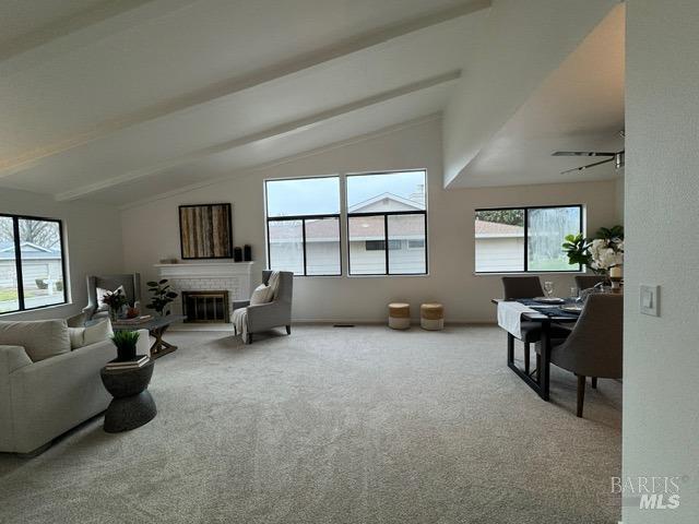 carpeted living room with vaulted ceiling with beams, a wealth of natural light, and a fireplace