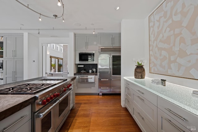 kitchen featuring built in appliances, gray cabinets, light hardwood / wood-style floors, and backsplash