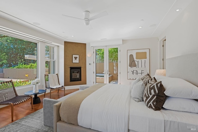 bedroom with a fireplace, wood-type flooring, access to outside, ceiling fan, and french doors