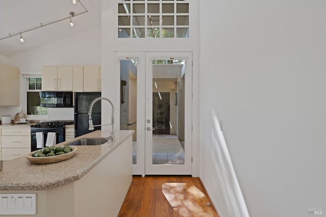 kitchen featuring high vaulted ceiling, sink, light hardwood / wood-style floors, black appliances, and french doors