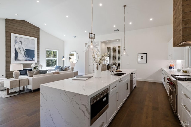 kitchen with hanging light fixtures, a kitchen island with sink, sink, and white cabinets