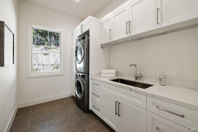 laundry area featuring cabinets, stacked washer / drying machine, and sink