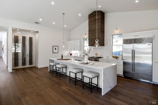 kitchen featuring sink, a kitchen island with sink, white cabinets, decorative light fixtures, and built in fridge