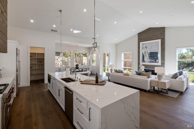 kitchen with pendant lighting, sink, light stone counters, and a center island with sink