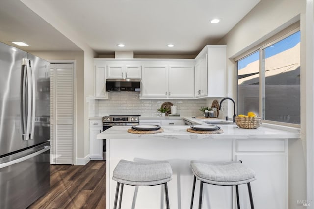 kitchen with sink, a breakfast bar area, appliances with stainless steel finishes, white cabinetry, and light stone counters