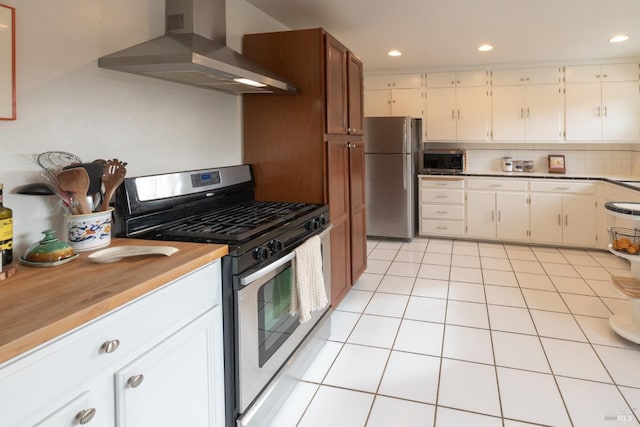 kitchen featuring light tile patterned flooring, appliances with stainless steel finishes, white cabinets, and wall chimney exhaust hood