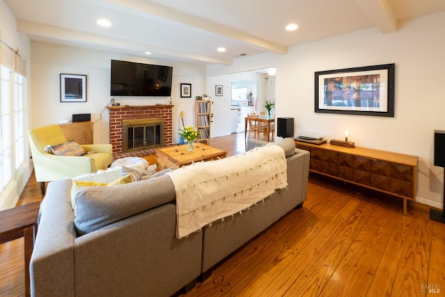 living room with wood-type flooring, beam ceiling, and a brick fireplace