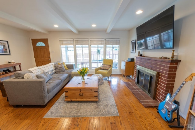 living room featuring a brick fireplace, beam ceiling, and light hardwood / wood-style flooring