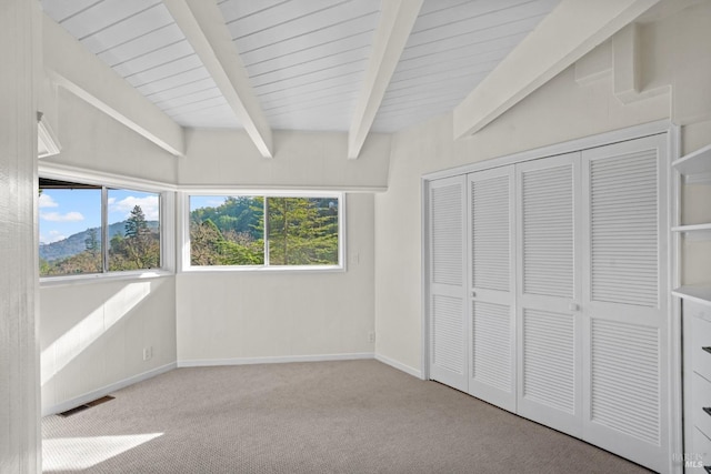 unfurnished bedroom with carpet, visible vents, beamed ceiling, and multiple windows