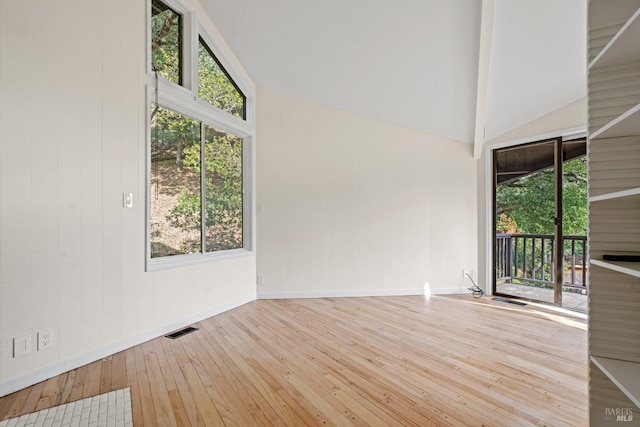 spare room featuring a healthy amount of sunlight, high vaulted ceiling, visible vents, and hardwood / wood-style floors