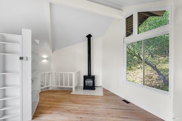 unfurnished living room featuring lofted ceiling with beams, a wood stove, wood finished floors, and visible vents