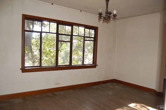 empty room featuring dark wood-type flooring, a wealth of natural light, and a chandelier