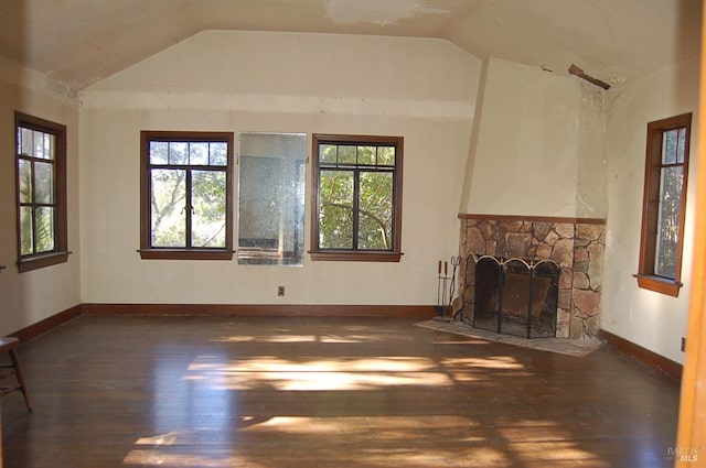 unfurnished living room with dark wood-type flooring, lofted ceiling, and a stone fireplace