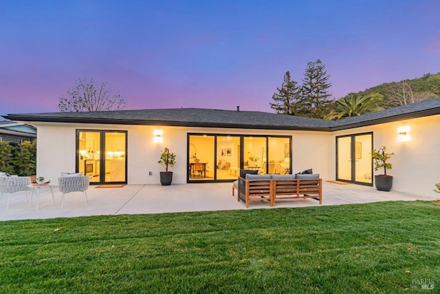 back house at dusk with an outdoor living space, a yard, and a patio area