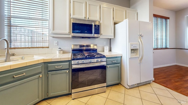 kitchen with light tile patterned flooring, sink, white cabinetry, tile countertops, and appliances with stainless steel finishes