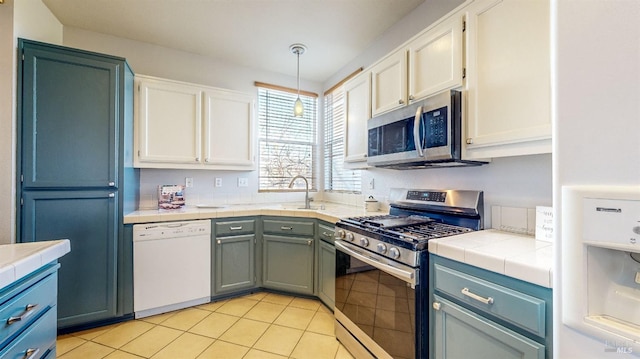 kitchen with appliances with stainless steel finishes, tile countertops, white cabinetry, sink, and hanging light fixtures