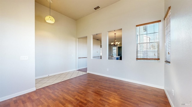 empty room with an inviting chandelier, wood-type flooring, and a high ceiling