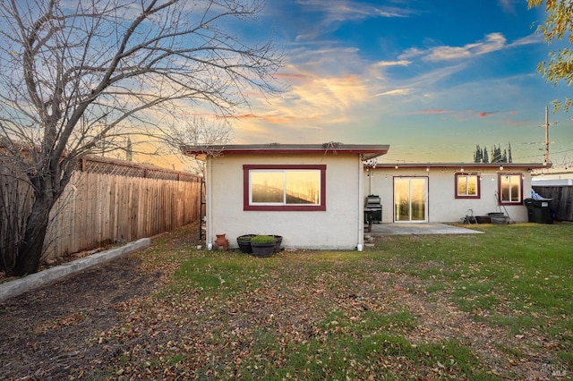 back house at dusk featuring a patio and a yard