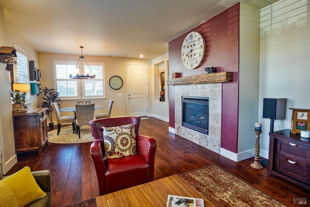 living room with dark hardwood / wood-style floors, a tile fireplace, and a notable chandelier