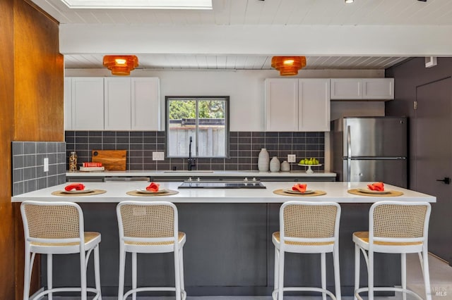 kitchen with light countertops, decorative backsplash, freestanding refrigerator, white cabinetry, and a sink