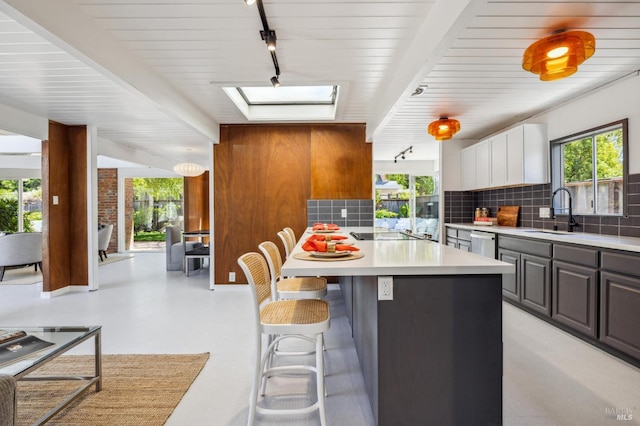 kitchen with a skylight, a breakfast bar area, a sink, light countertops, and stainless steel dishwasher