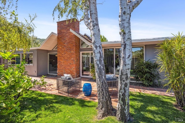 rear view of property with a patio area, a lawn, and a chimney