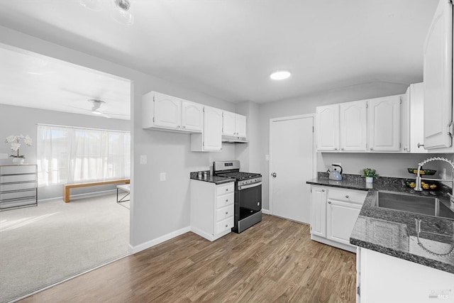 kitchen featuring sink, dark stone countertops, white cabinets, stainless steel range with gas cooktop, and light wood-type flooring