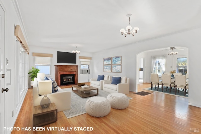 living room with an inviting chandelier, a brick fireplace, and light wood-type flooring