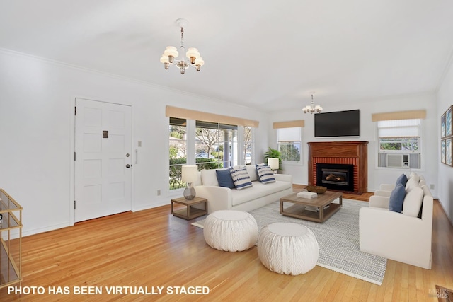 living room with a notable chandelier, wood-type flooring, a fireplace, and ornamental molding