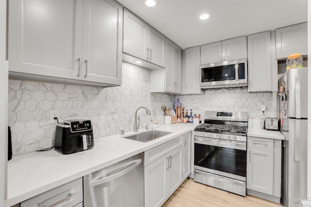 kitchen featuring stainless steel appliances, sink, light wood-type flooring, and decorative backsplash