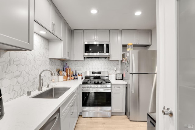 kitchen with tasteful backsplash, stainless steel appliances, sink, and light wood-type flooring