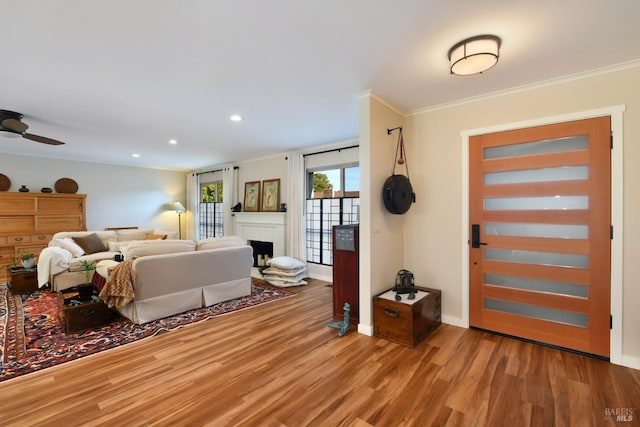 interior space featuring crown molding, a brick fireplace, ceiling fan, and light hardwood / wood-style flooring