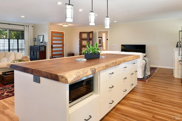 kitchen with butcher block counters, white cabinetry, light hardwood / wood-style floors, a kitchen island, and decorative light fixtures