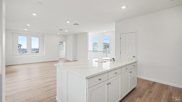 kitchen with white cabinetry, light stone counters, light hardwood / wood-style flooring, a kitchen island, and a healthy amount of sunlight