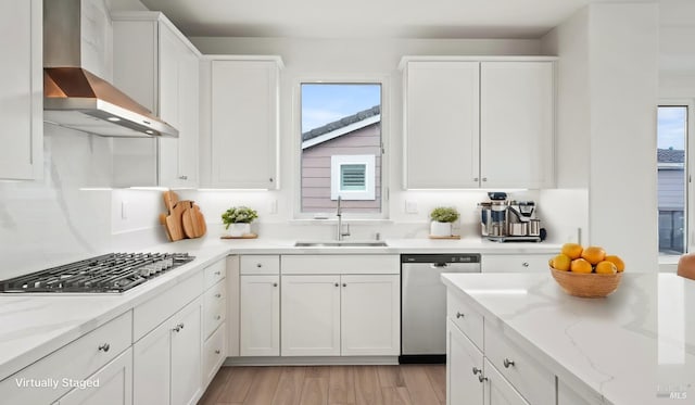 kitchen with appliances with stainless steel finishes, wall chimney exhaust hood, sink, and white cabinets