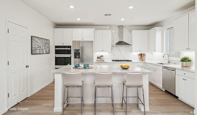 kitchen with white cabinets, a kitchen island, wall chimney exhaust hood, and appliances with stainless steel finishes