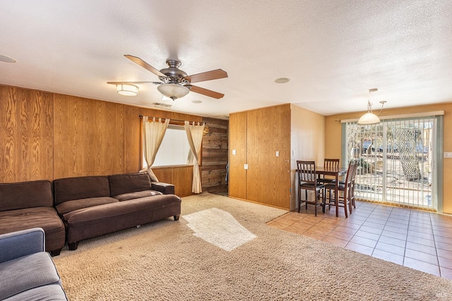 living room featuring ceiling fan, light carpet, a textured ceiling, and wood walls