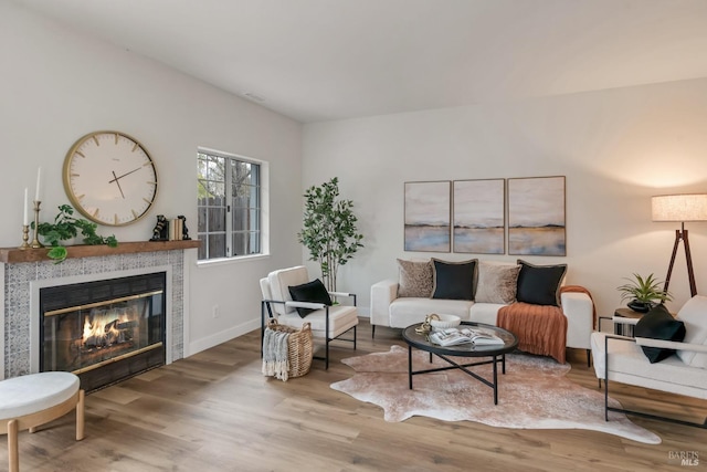 living room featuring visible vents, baseboards, wood finished floors, and a tiled fireplace